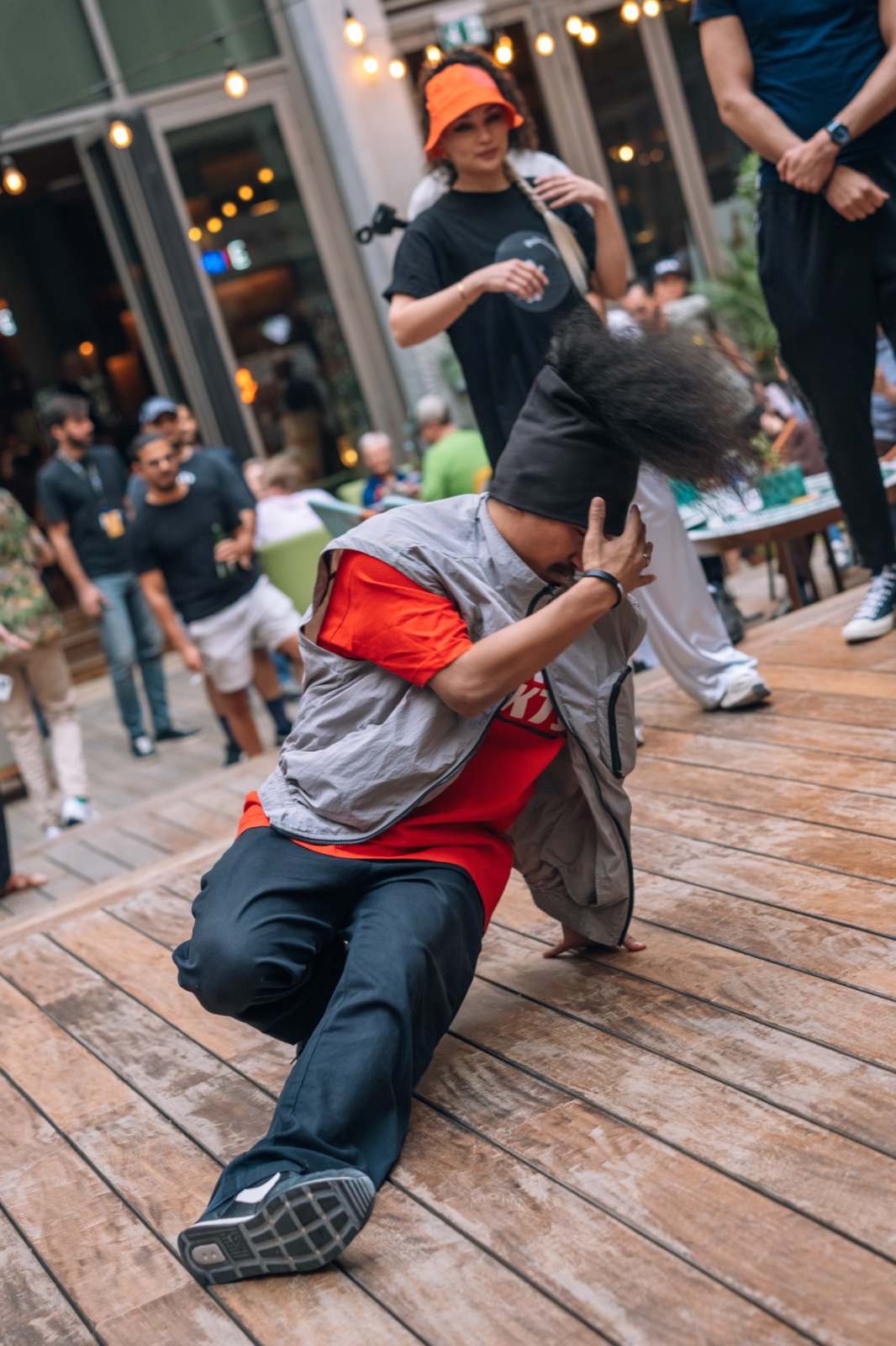 A breakdancer in a red and grey outfit mid-move on a wooden stage.