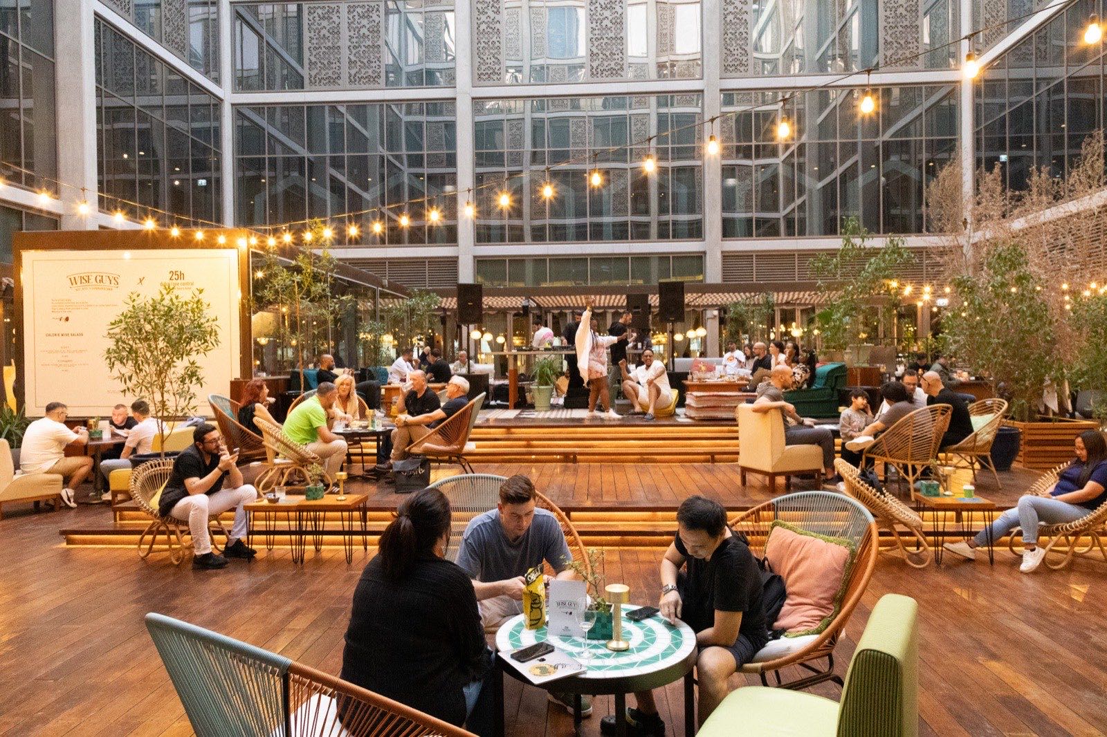A wide terrace with people at tables under strings of lights.