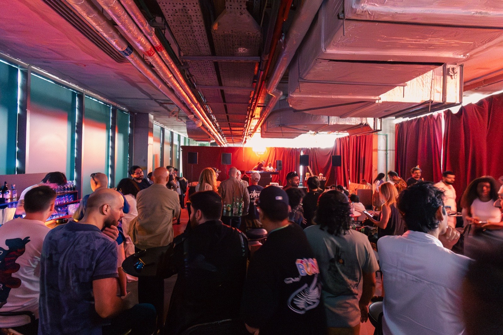 A packed room with people gathered in front of red curtains.