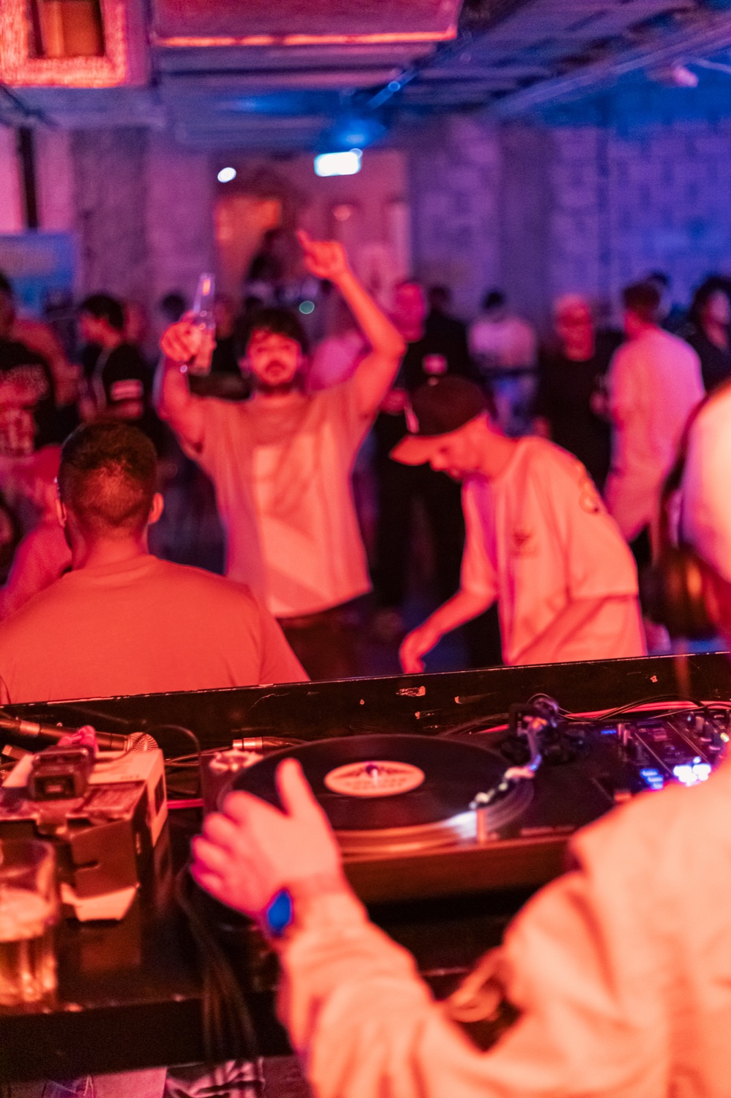 People dancing behind the turntables in coloured light.