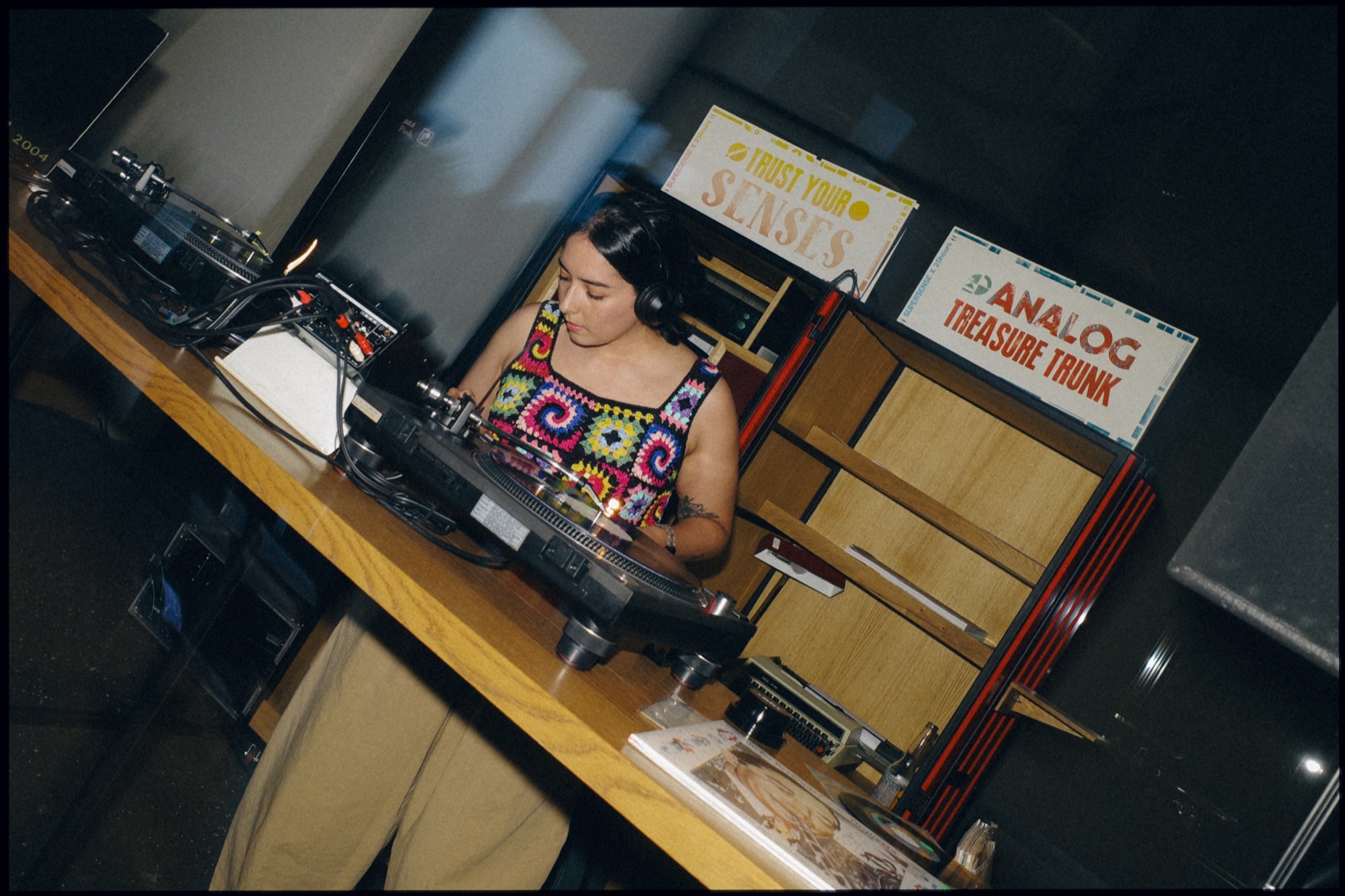 A DJ at the decks seen from above, beside an Analog Treasure Trunk sign.