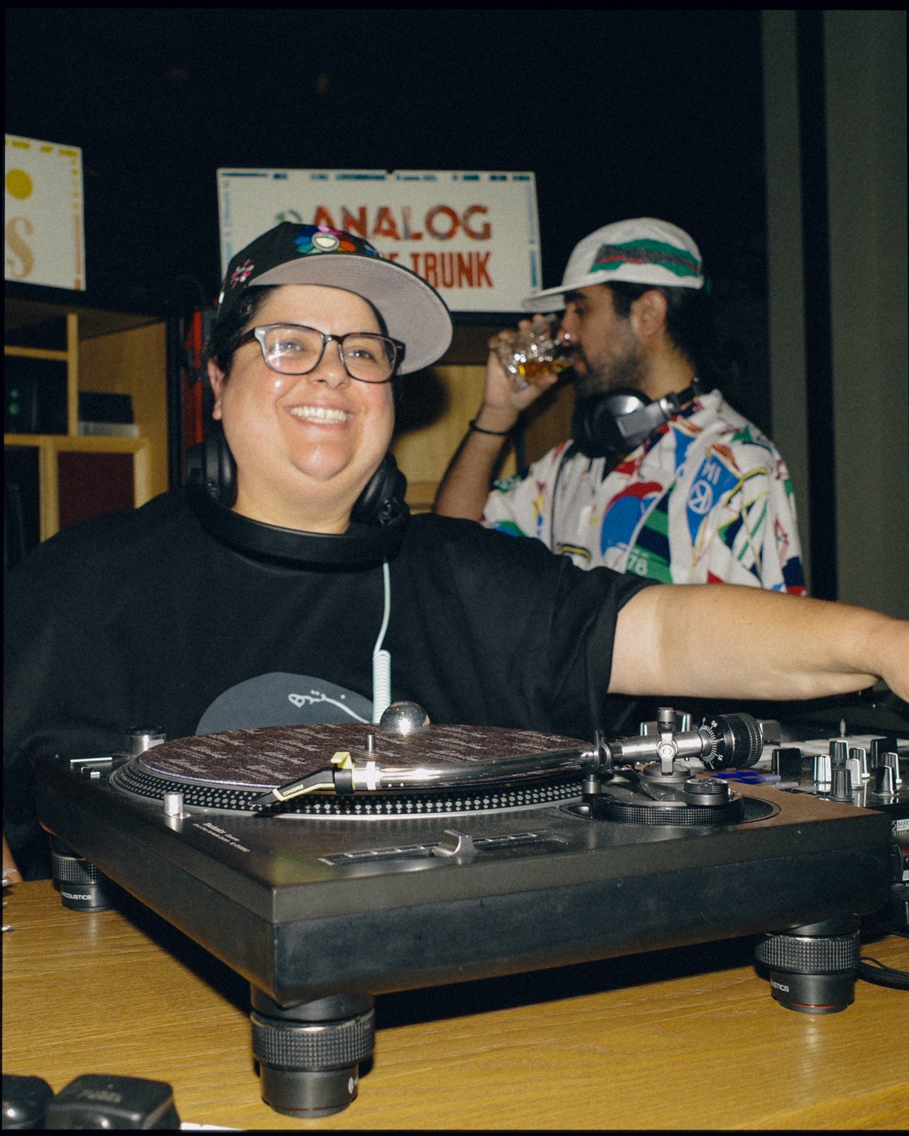 A DJ in glasses and a cap smiling at the turntables.