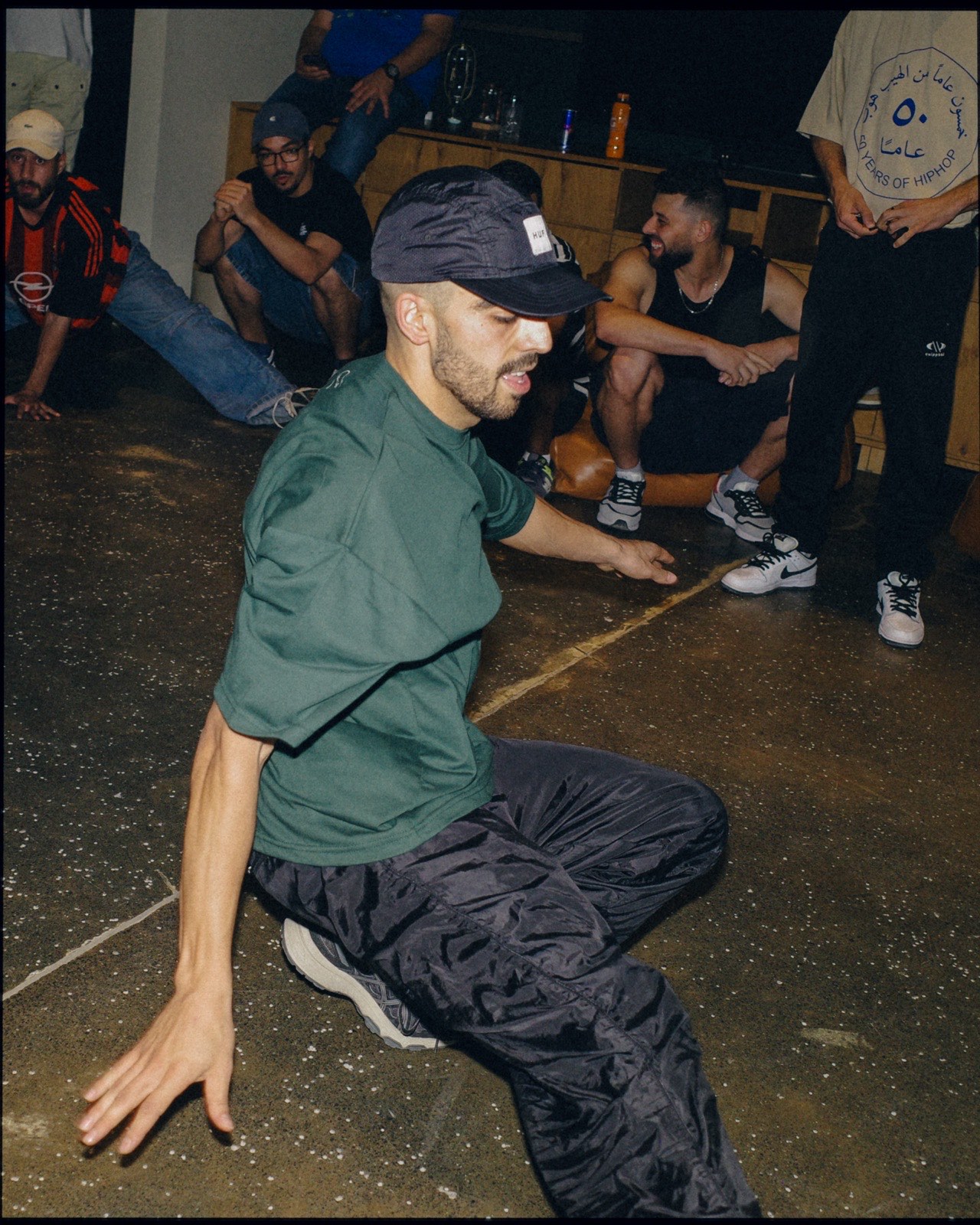 A breakdancer mid-move on the floor as people watch from the side.