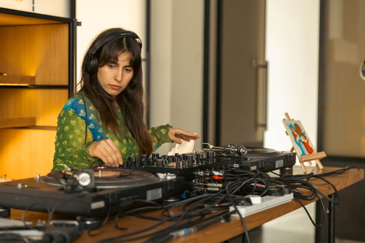 A DJ in headphones at the mixer between two turntables.